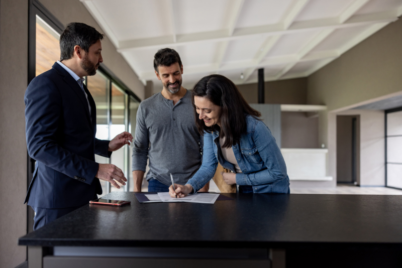 Couple buying a house and signing the deed in front of their real estate agent